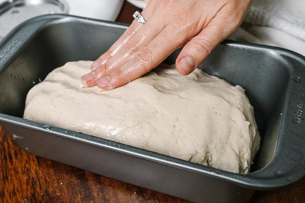 Gluten-free bread dough being pressed down in a tin